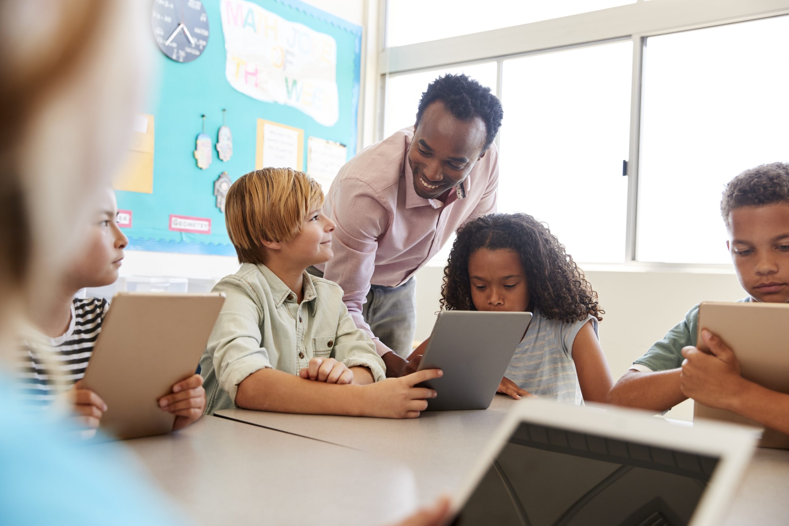 african american teacher overseeing four students using tablets in a classroom